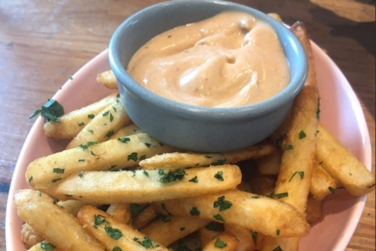 Image showing a bowl of homemade Freddy's Fry Sauce alongside a plate of crispy golden fries, with fresh herbs sprinkled on top for garnish.