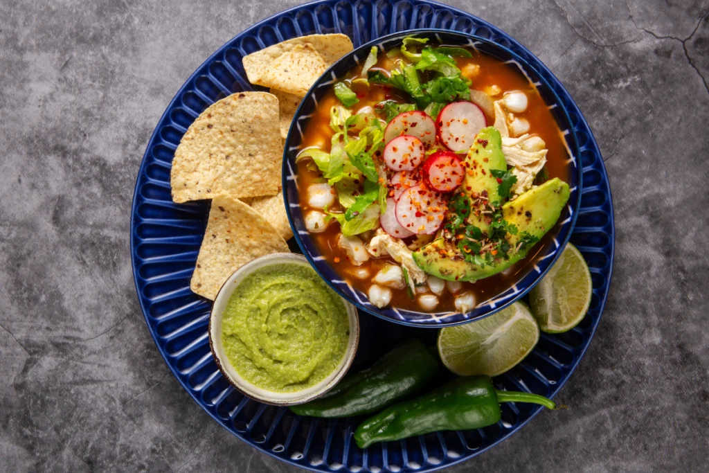 homemade taco soup garnished with shredded cheese, diced avocado, and a sprinkle of cilantro, served with a side of crispy tortilla chips